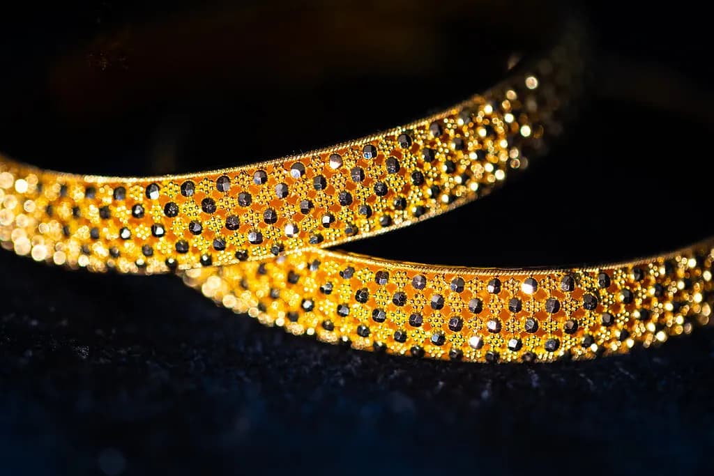 Two gold bangles studded with small dark stones on a dark background