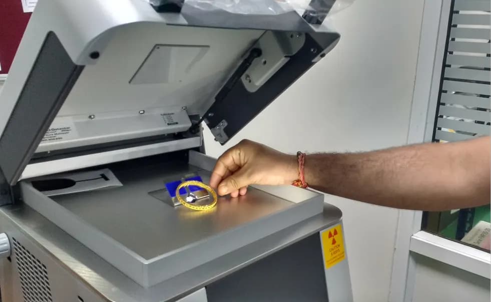 A hand placing a gold bangle into an XRF karat testing machine to check its purity