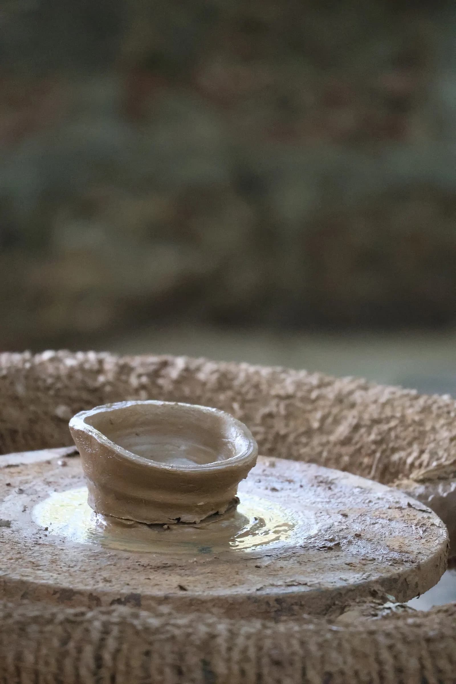 A small clay pot being shaped by hand on a traditional potter's wheel in India