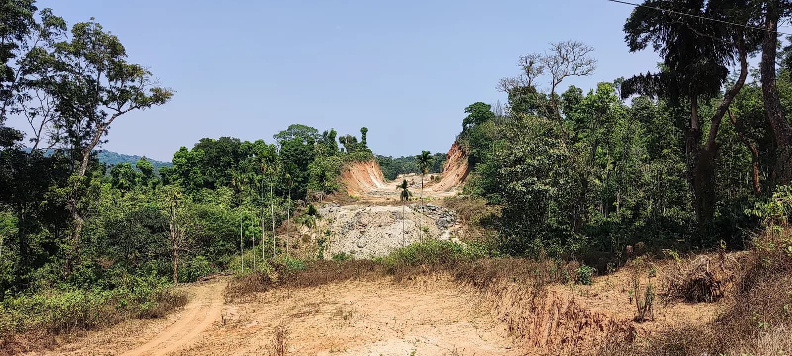 A new road being cut through forested hills in India, with excavated red earth and a bed of rubble