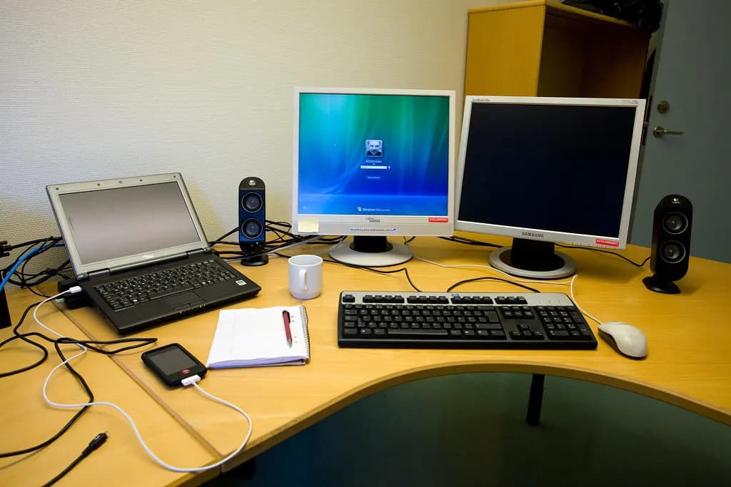 Office desk with a laptop, two monitors, keyboard, notebook and phone