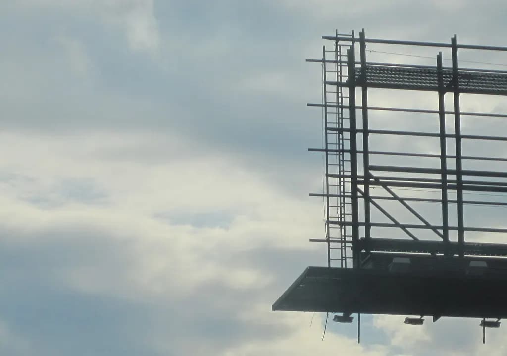 The steel frame and catwalk of an empty roadside billboard against a cloudy sky