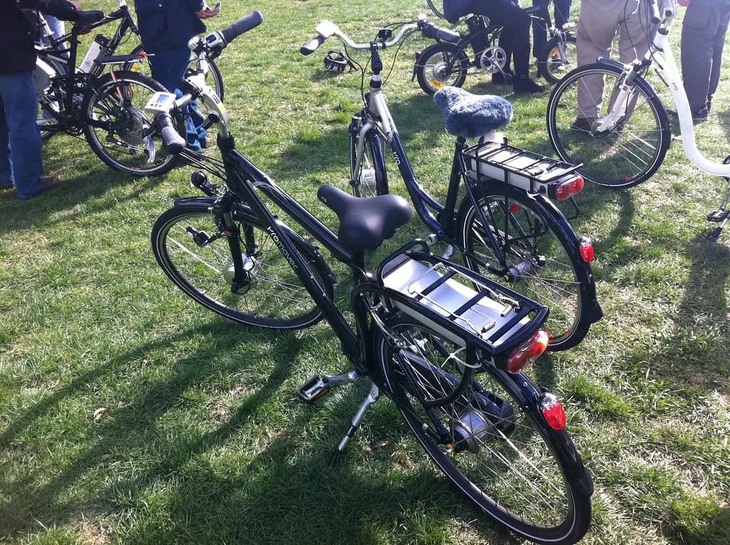 Two electric bicycles on grass with the battery pack fitted behind the seat on the rear carrier
