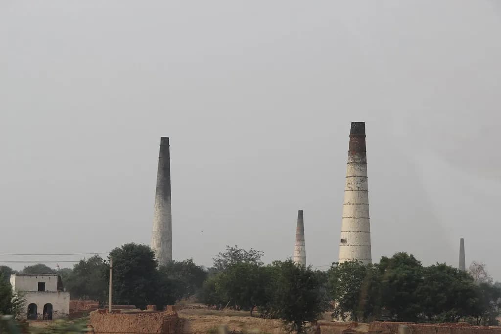 Tall brick kiln chimneys rising above fields and trees in the Indian countryside
