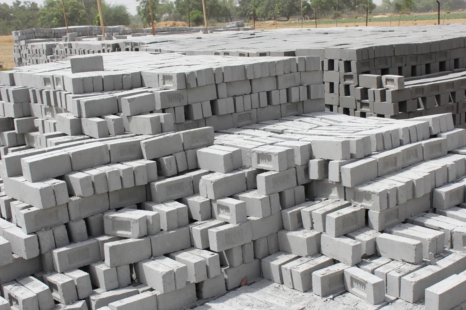 Rows of grey fly ash bricks stacked in a yard to cure