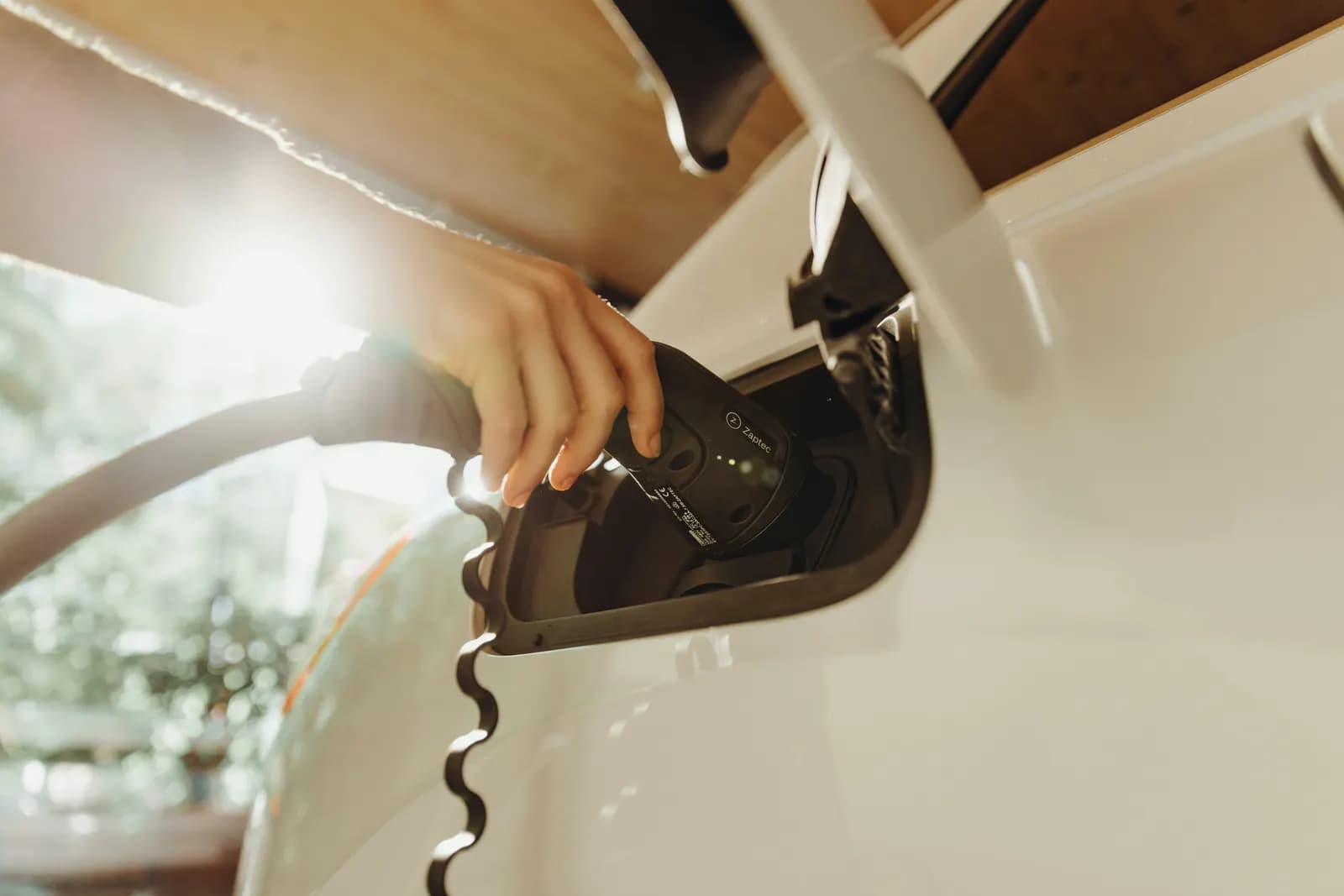 A hand plugging a charging cable into a white electric car