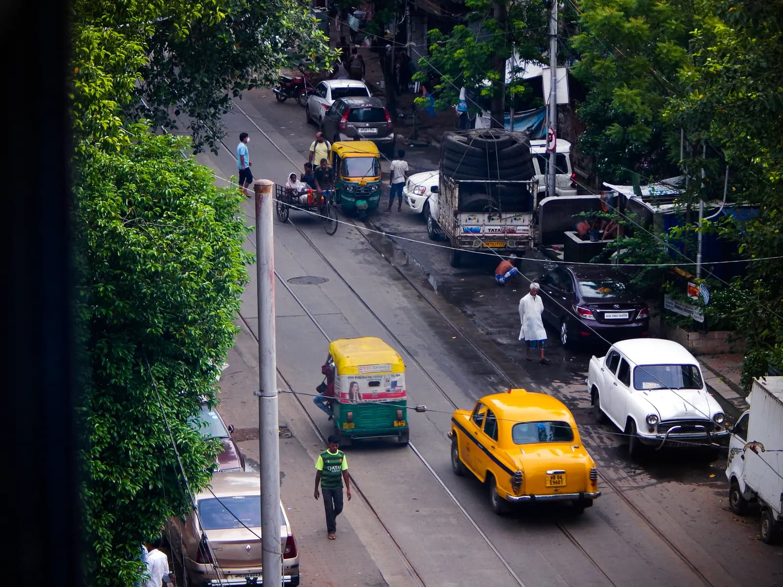 A Kolkata street with yellow taxis, an auto-rickshaw and private cars