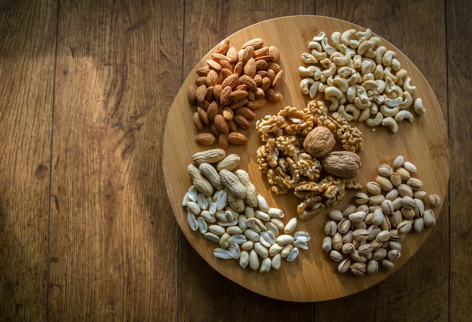 Almonds, cashews, walnuts and pistachios in separate heaps on a round wooden board