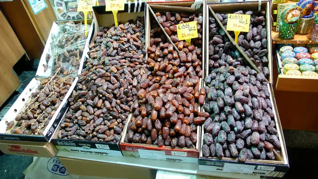 Trays of loose dried dates of different varieties with price tags at a market stall