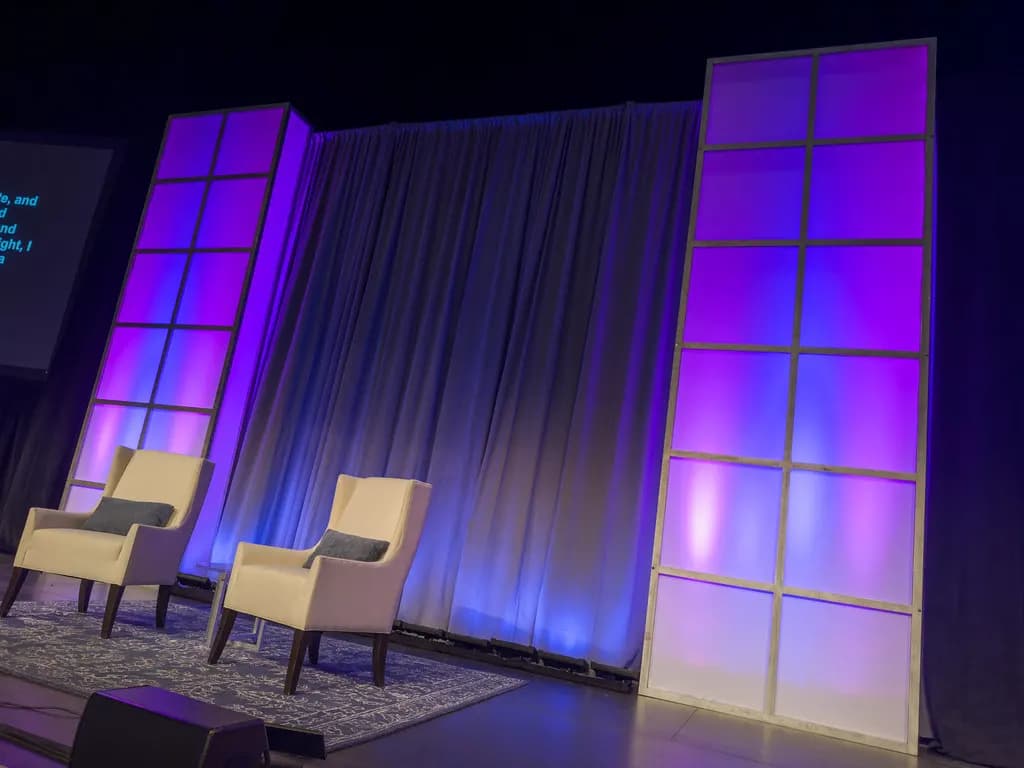 A conference stage with two armchairs, a projection screen and panels lit in purple