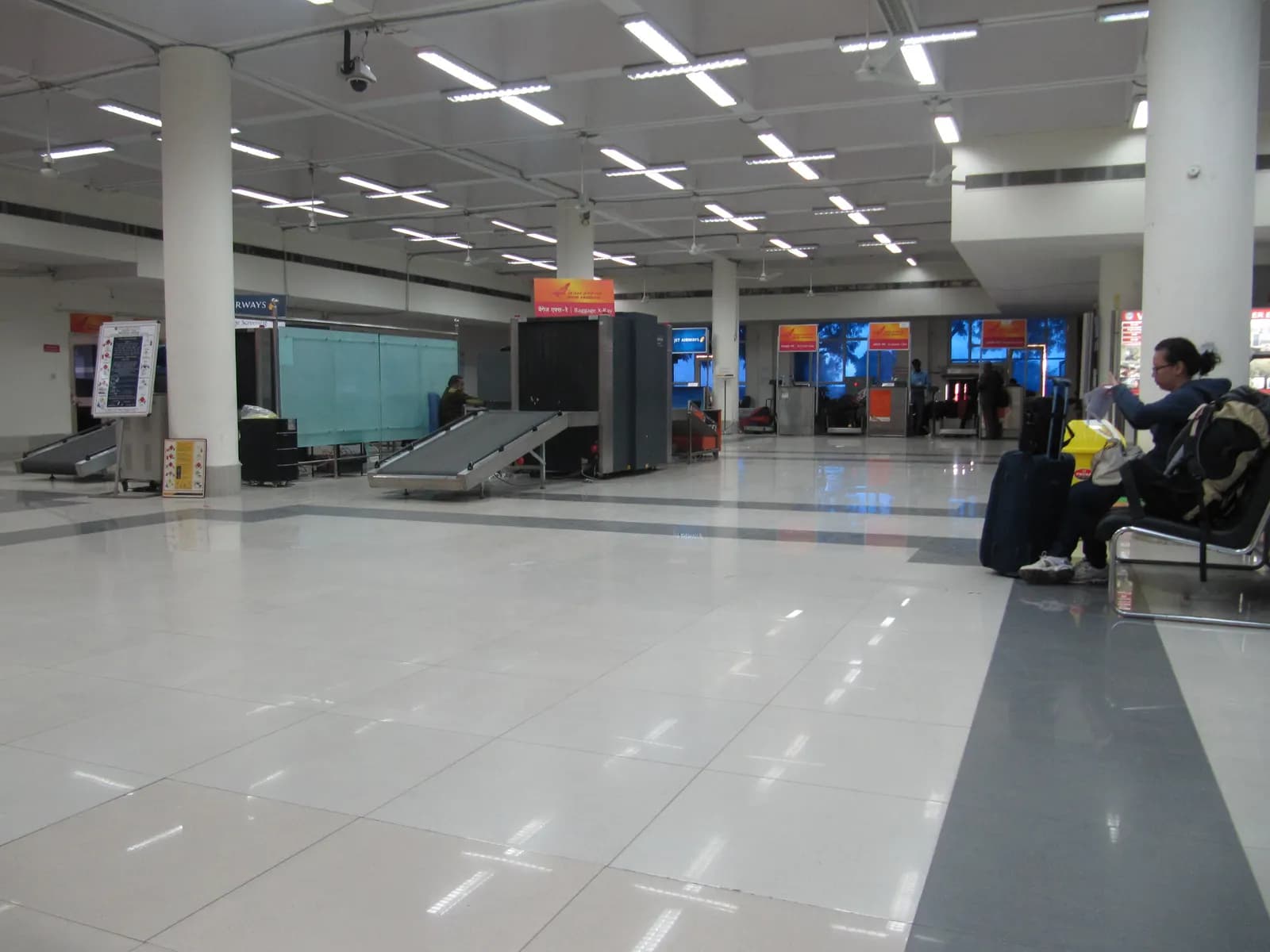 Check-in hall and baggage screening machines at Jodhpur airport with a passenger waiting on a bench