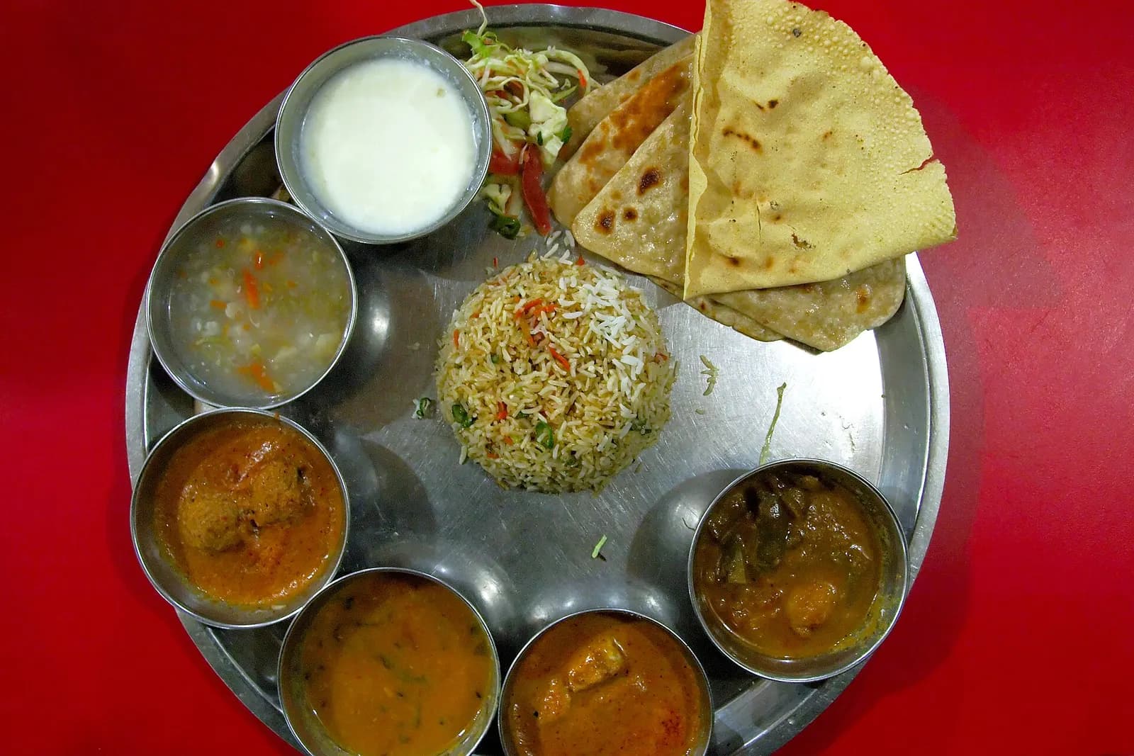 A restaurant thali with rice, chapatis, curries, dal and curd on a steel plate