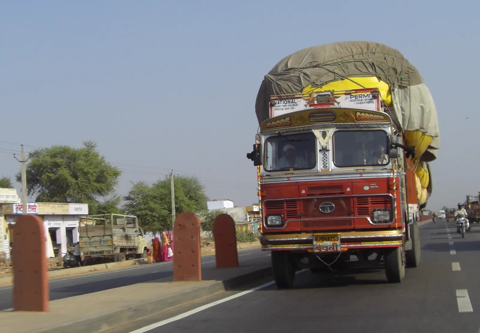 A fully loaded Indian goods truck with a tarpaulin-covered load driving on a highway