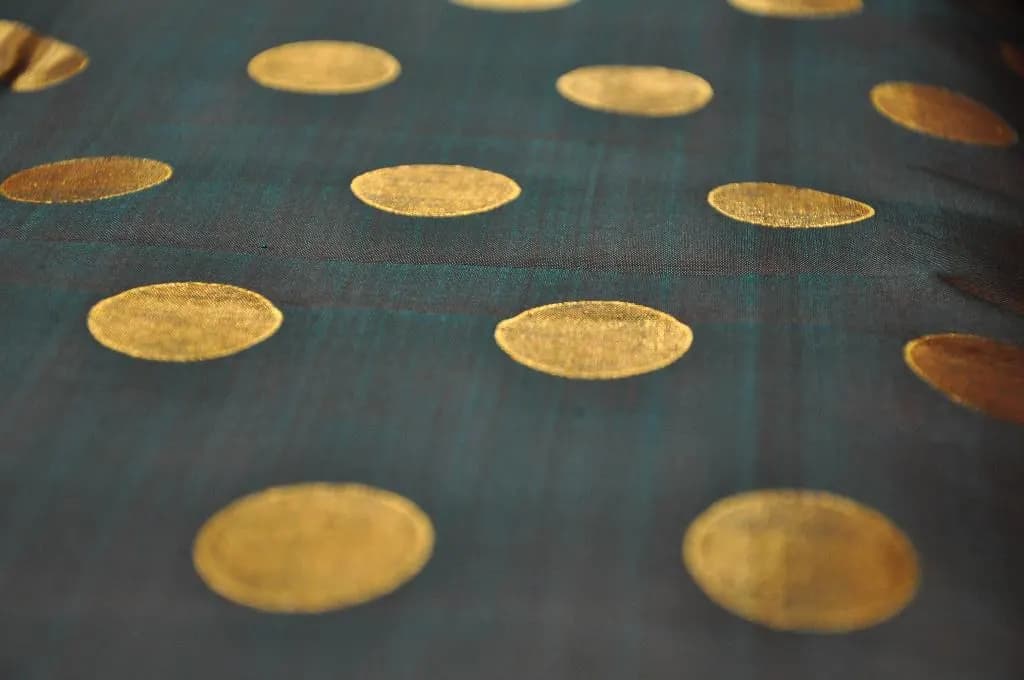 Close-up of a dark green silk saree woven with gold zari polka dots, photographed at a saree shop