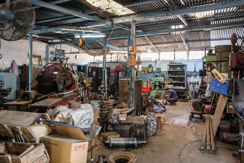 Inside a vehicle service workshop in India with engine parts, tools and boxes of spares on the floor