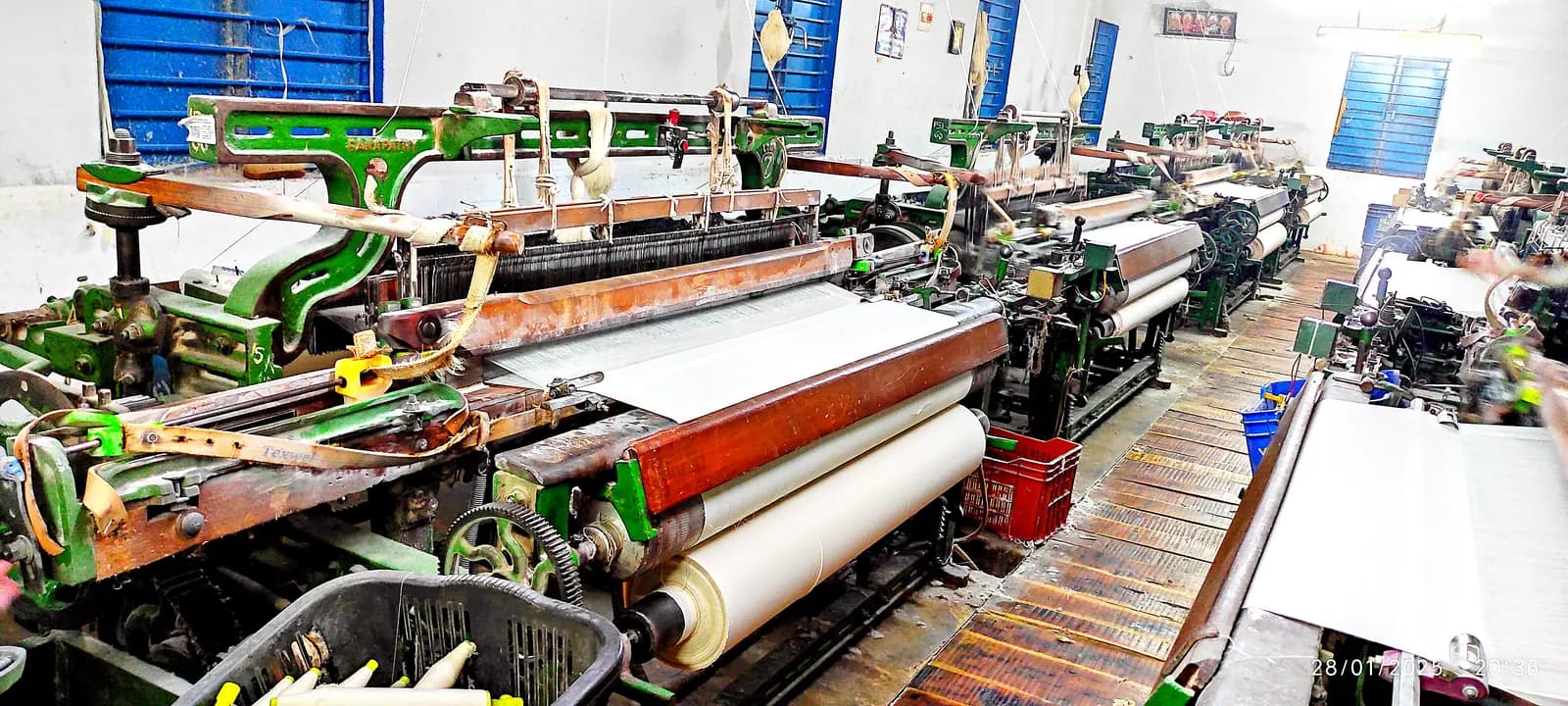 Rows of powerlooms weaving white fabric inside a powerloom shed in India