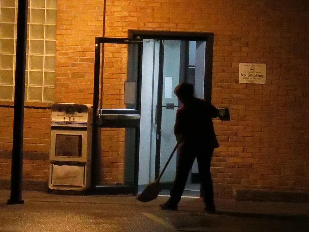 A cleaning worker sweeping outside a building entrance in the evening