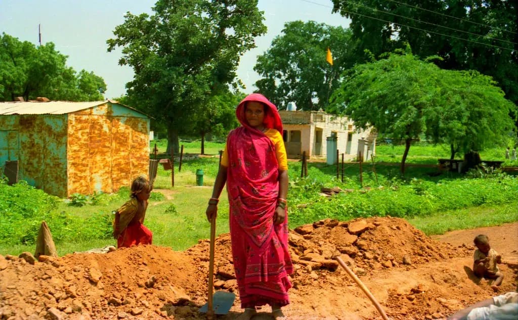 A woman worker in a red sari digging earth on a roadside work site in rural India