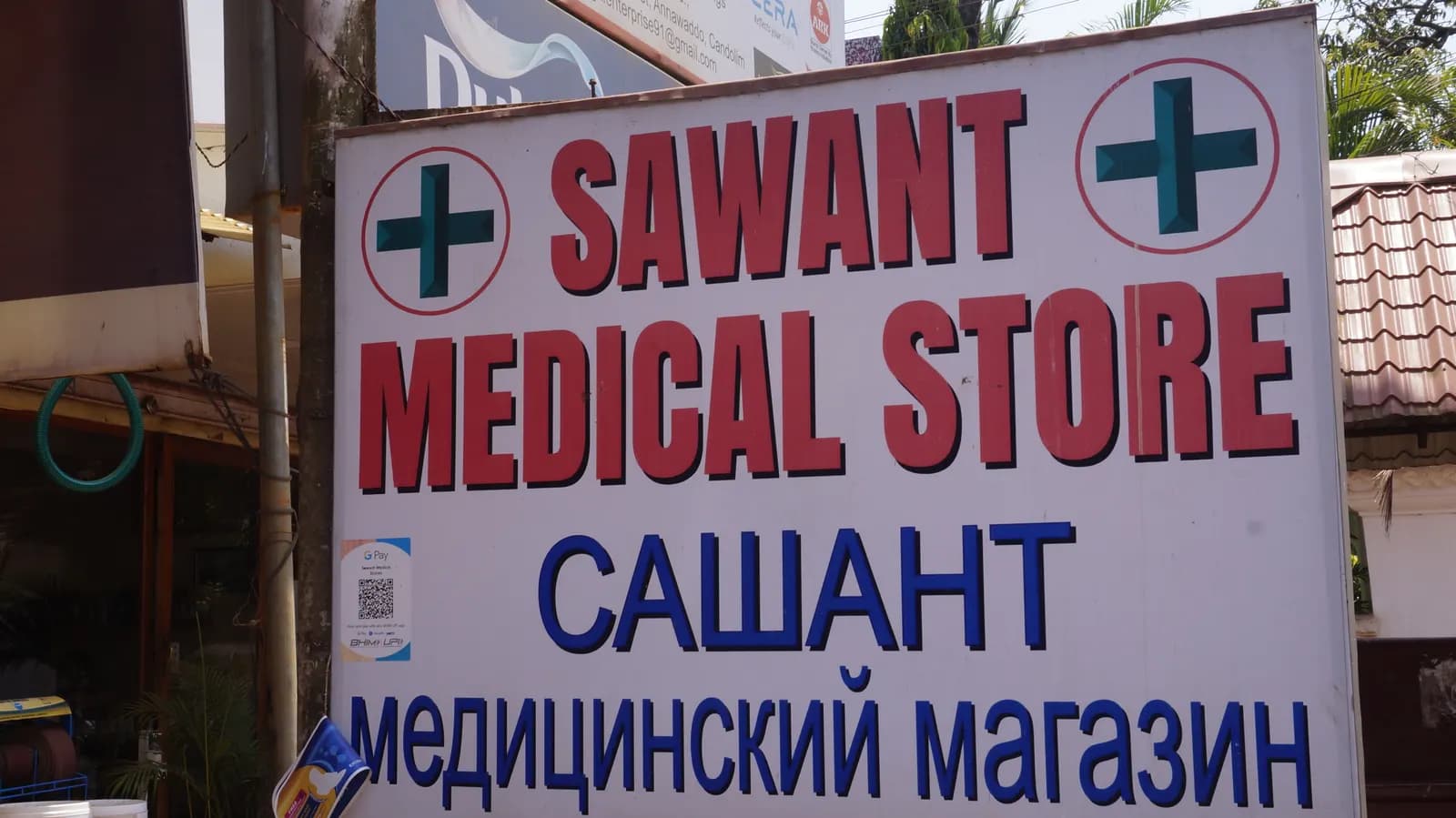 Signboard of a neighbourhood medical store in Goa with green cross symbols, in English and Russian