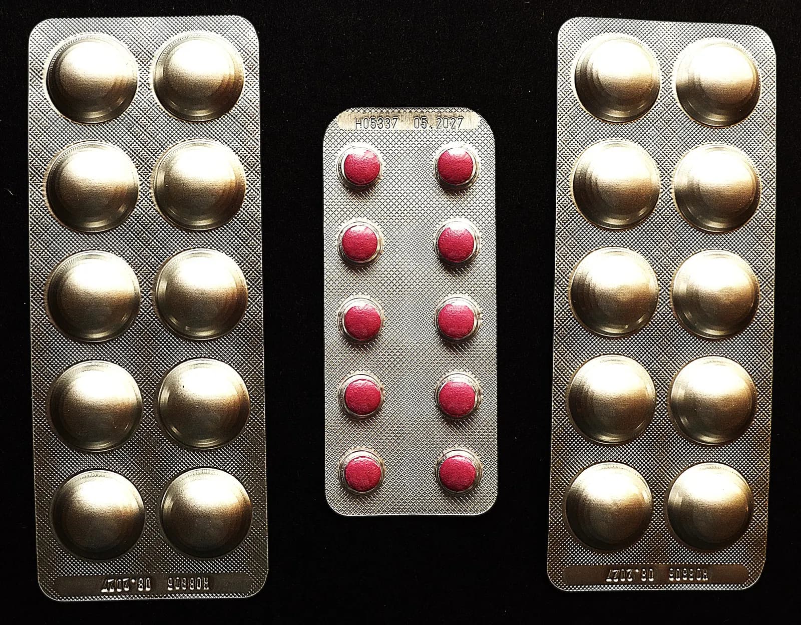 Three blister strips of tablets laid side by side on a black background, with batch and expiry details printed on the foil
