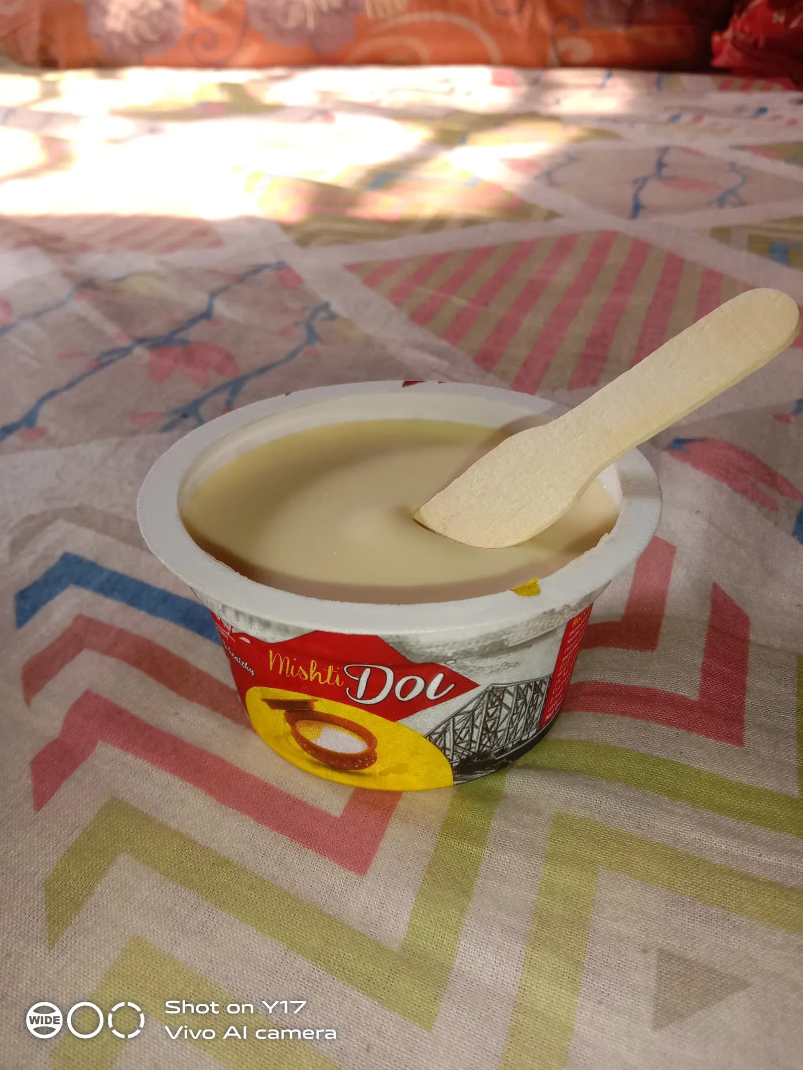 A sealed retail cup of sweet curd (misti doi) with a wooden spoon