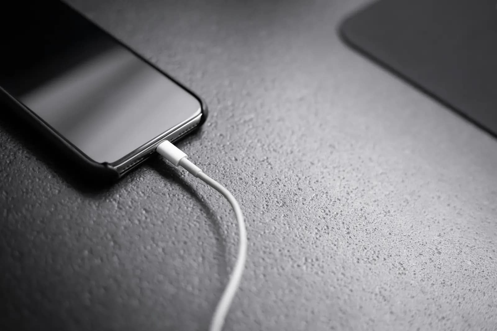 A black smartphone connected to a charging cable