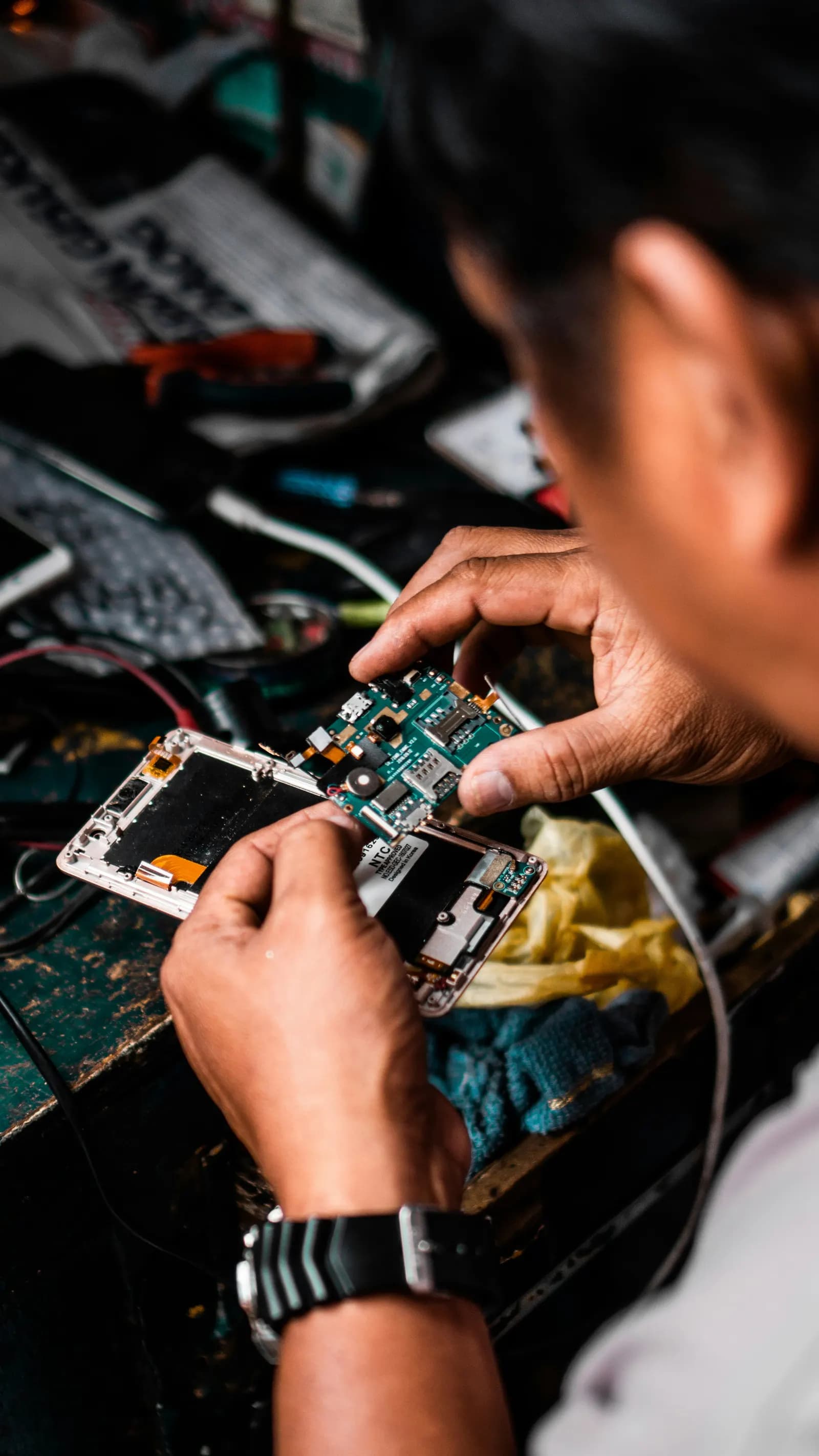 A technician repairing a smartphone circuit board at a workbench