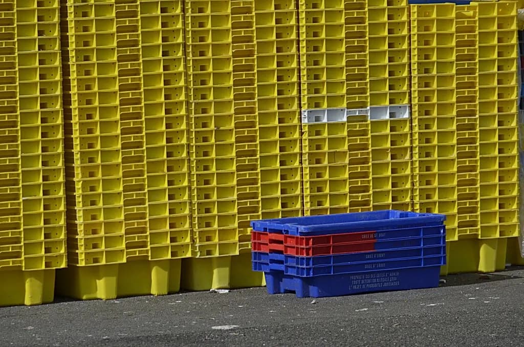 Tall stacks of yellow plastic crates with a few blue and red crates in front
