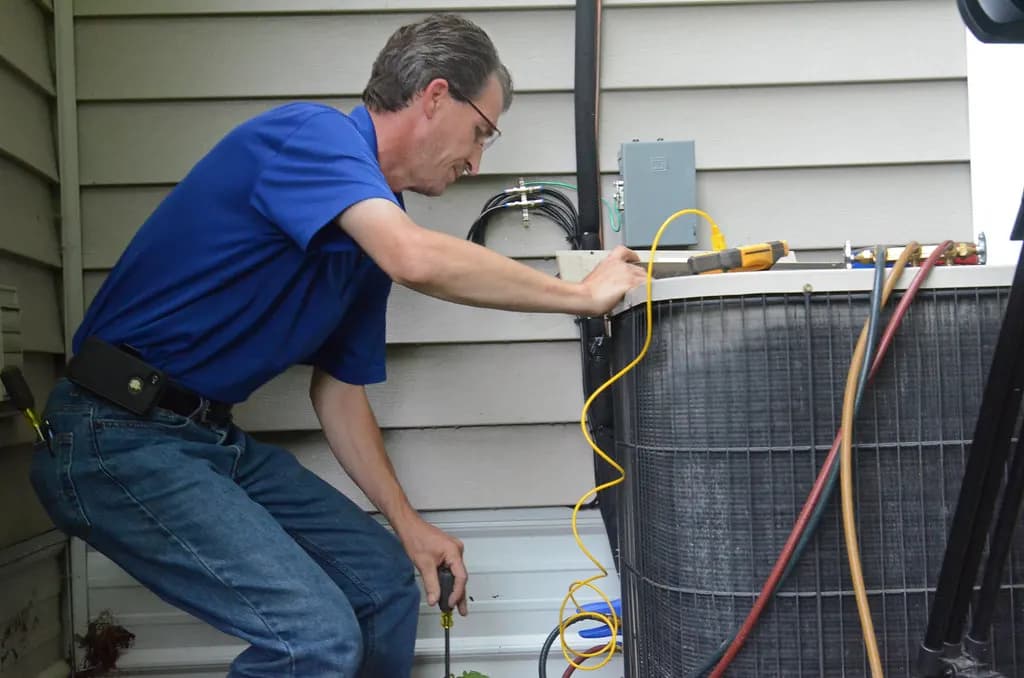 A technician connecting gauges to an outdoor air-conditioning unit during servicing