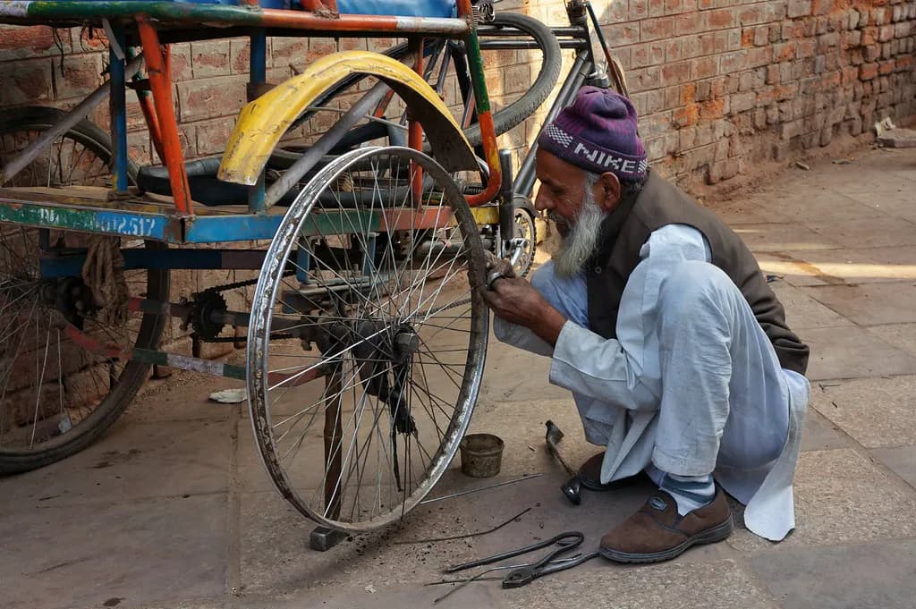 A roadside mechanic in Delhi crouching to repair the wheel of a cycle rickshaw