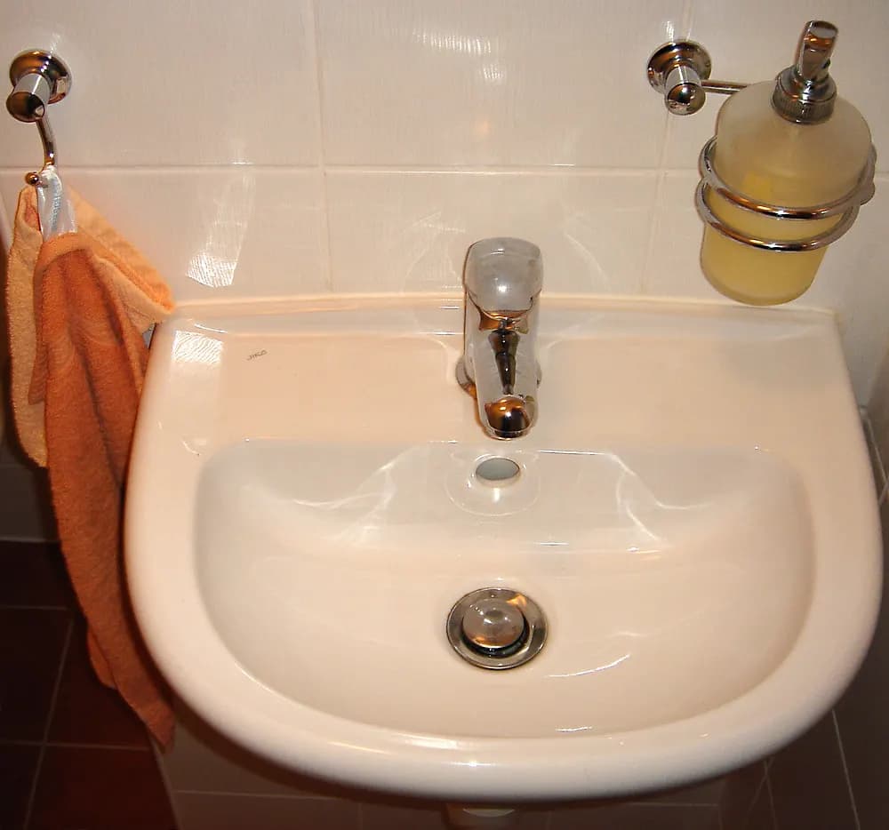 A white wall-hung ceramic wash basin with a chrome single-lever tap and soap dispenser in a tiled bathroom