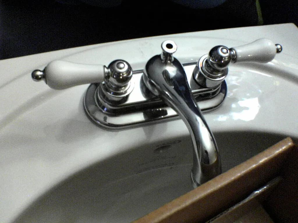 A chrome-plated two-handle basin mixer tap mounted on a white ceramic basin before installation