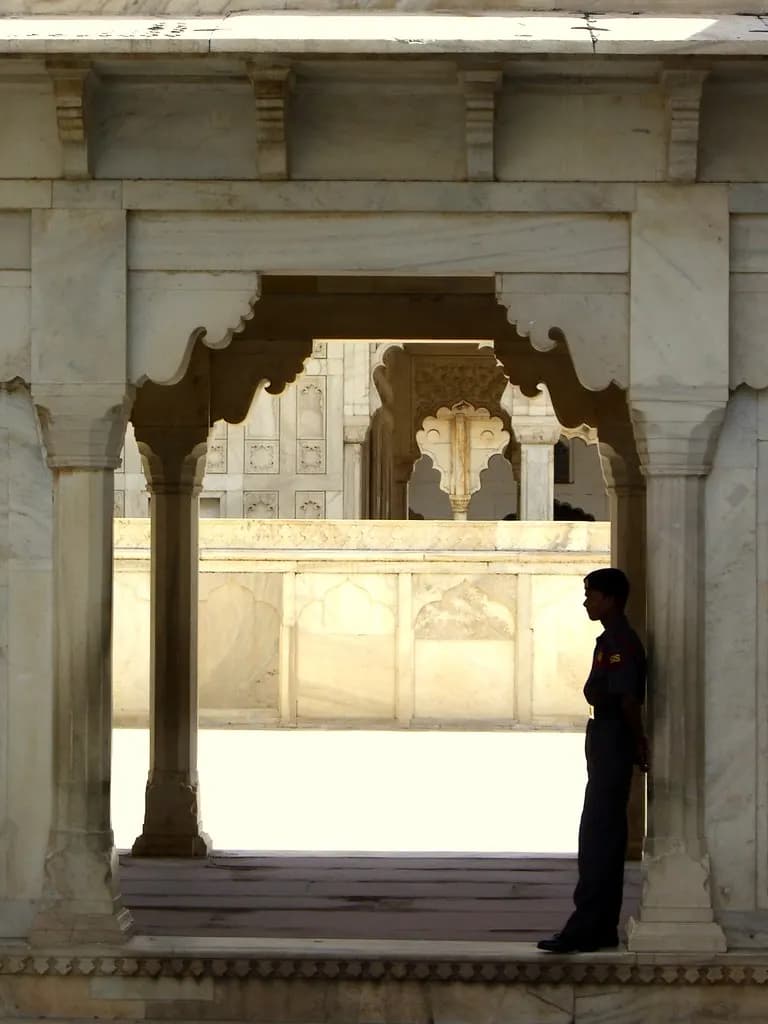 A uniformed security guard standing beside a marble archway at Agra Fort