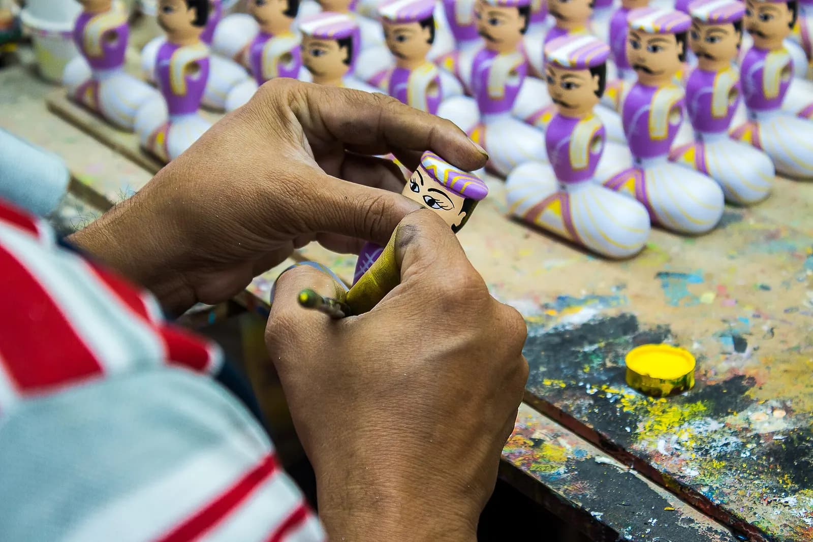 An artisan's hands painting rows of wooden Channapatna dolls at a workbench
