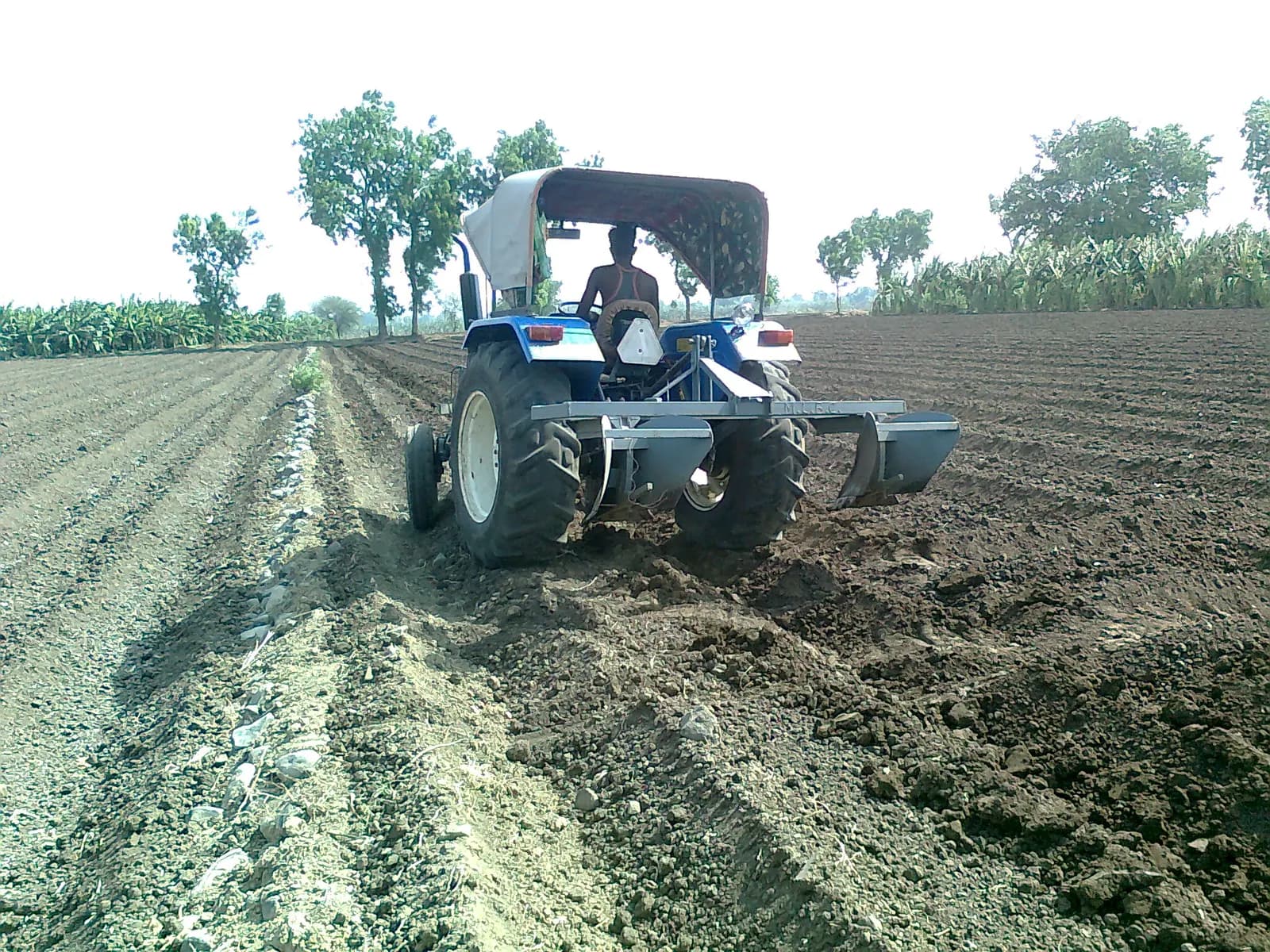 A farmer driving a tractor with a ridging implement across a ploughed field in Chinawal, Maharashtra