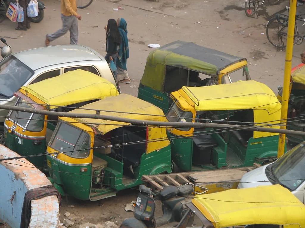 A line of green and yellow CNG auto-rickshaws parked on a street in Delhi