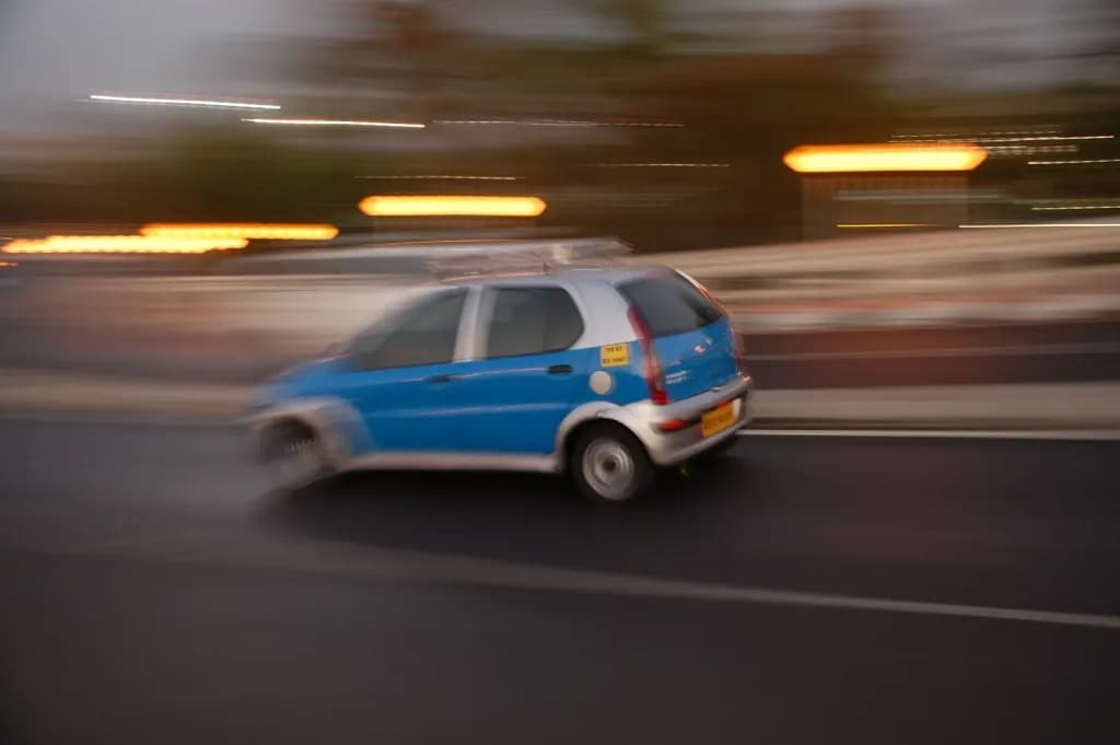 A blue air-conditioned cab driving along a Mumbai road, blurred by motion