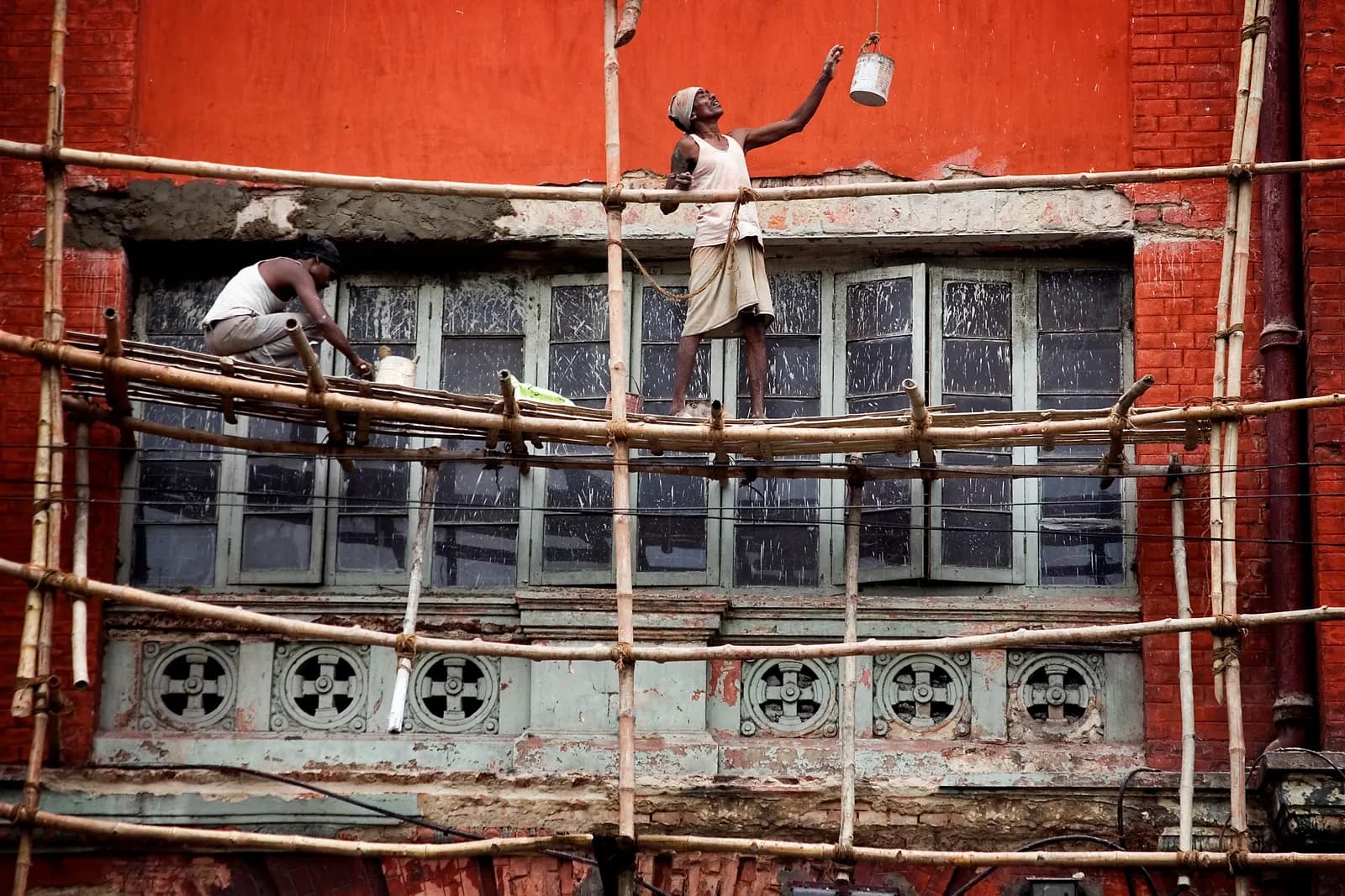 Two workers on bamboo scaffolding repairing and painting the facade of an old building in Kolkata