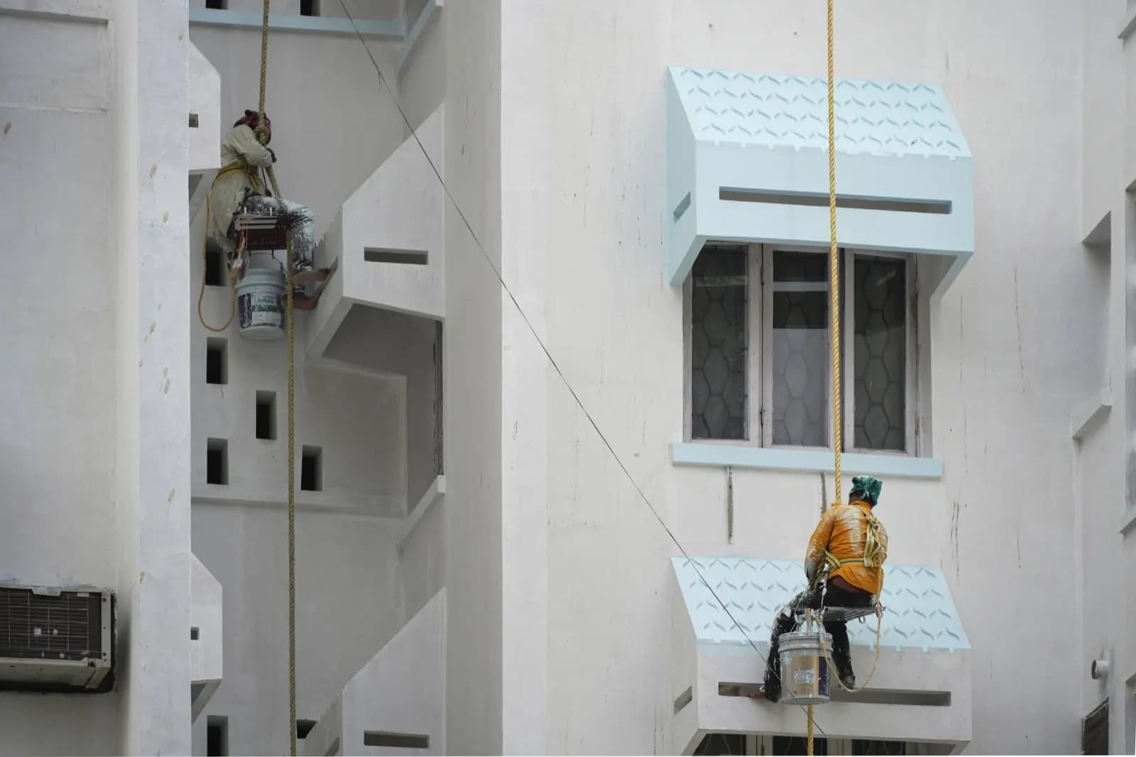 Two painters suspended on ropes painting the exterior wall of a building in Fort Kochi, Kerala