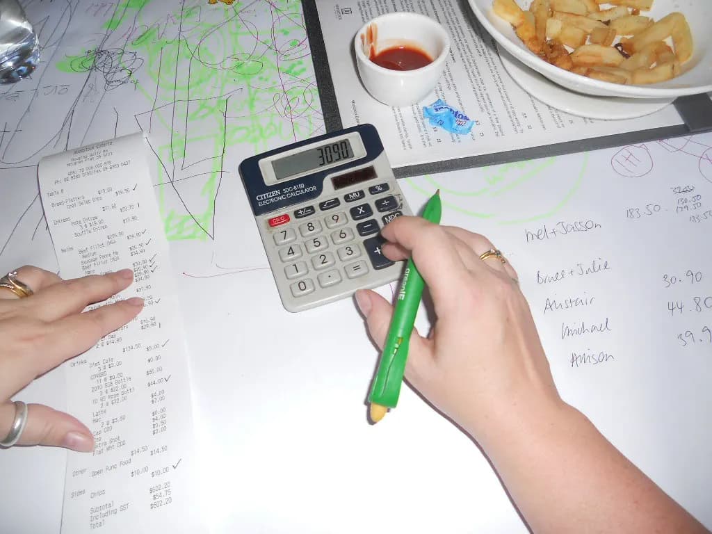 Hands cross-checking a printed bill against a calculator and handwritten notes