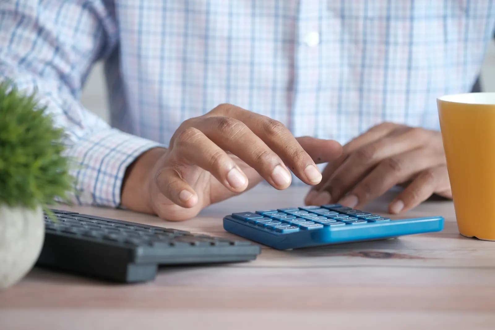 A person working on a calculator at a desk with papers and a coffee mug