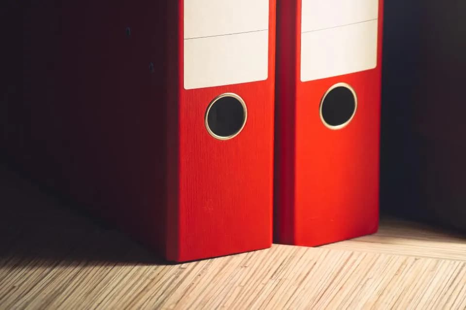 Two red lever-arch files standing on a wooden floor