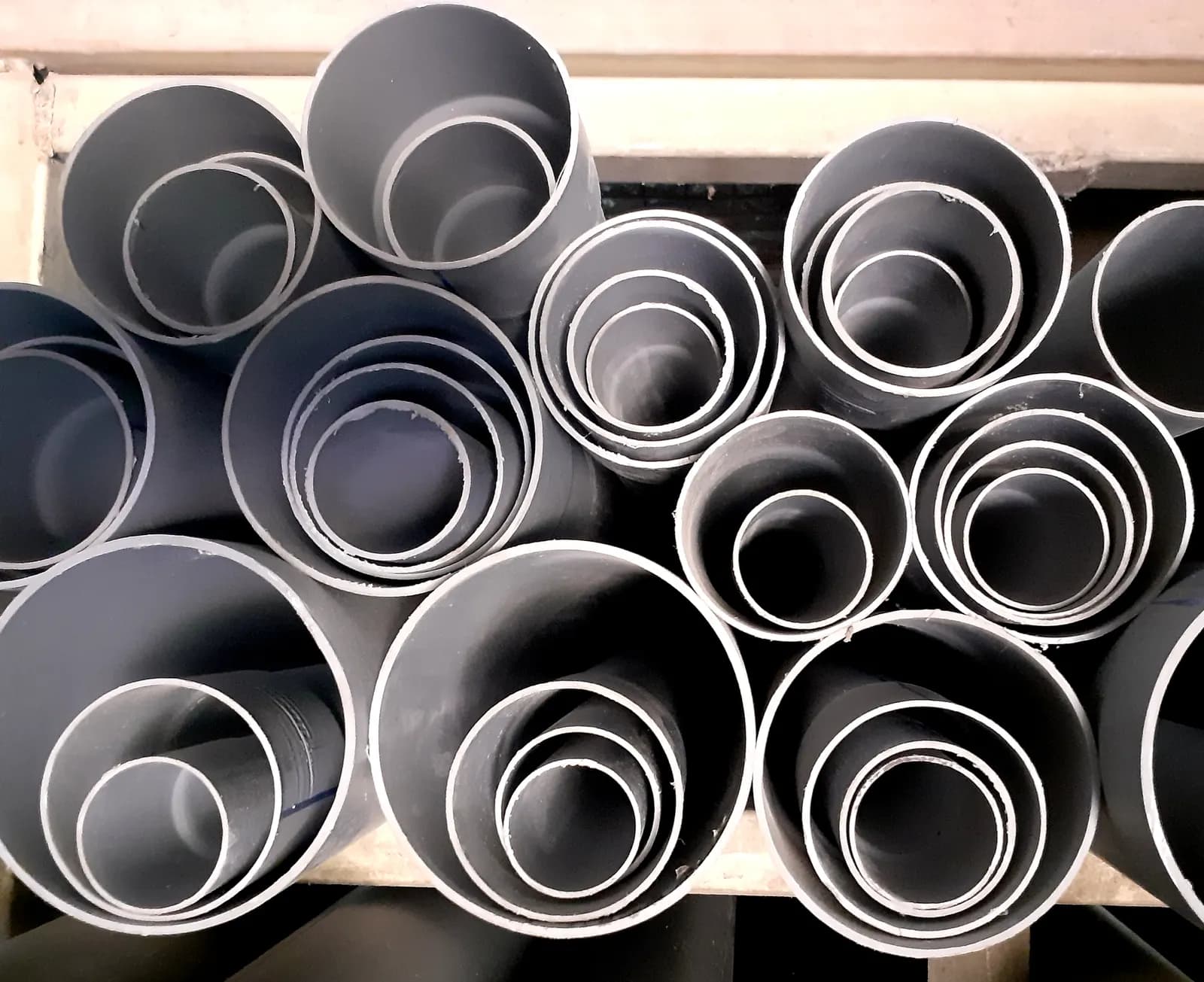Grey PVC pipes of different diameters stacked end-on on a shelf, seen from the open ends
