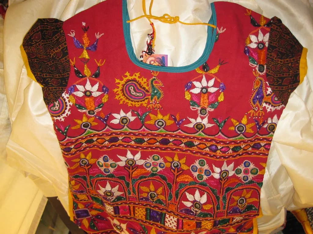 A red cotton kurti with Kutchi embroidery laid flat and photographed against a plain background