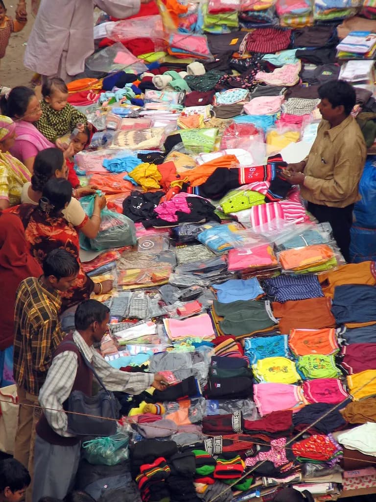 Shoppers browsing piles of colourful clothes on stalls at a crowded street market in Delhi
