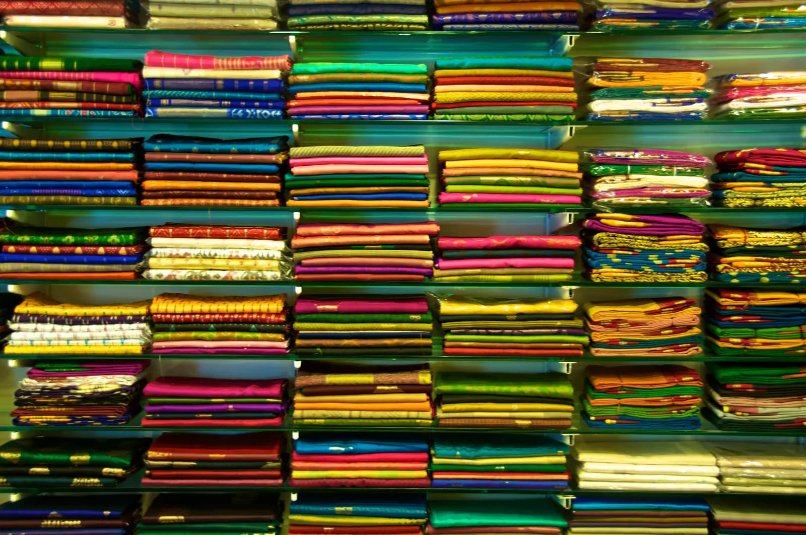 Floor-to-ceiling shelves in an Indian saree shop stacked with folded sarees in dozens of colours