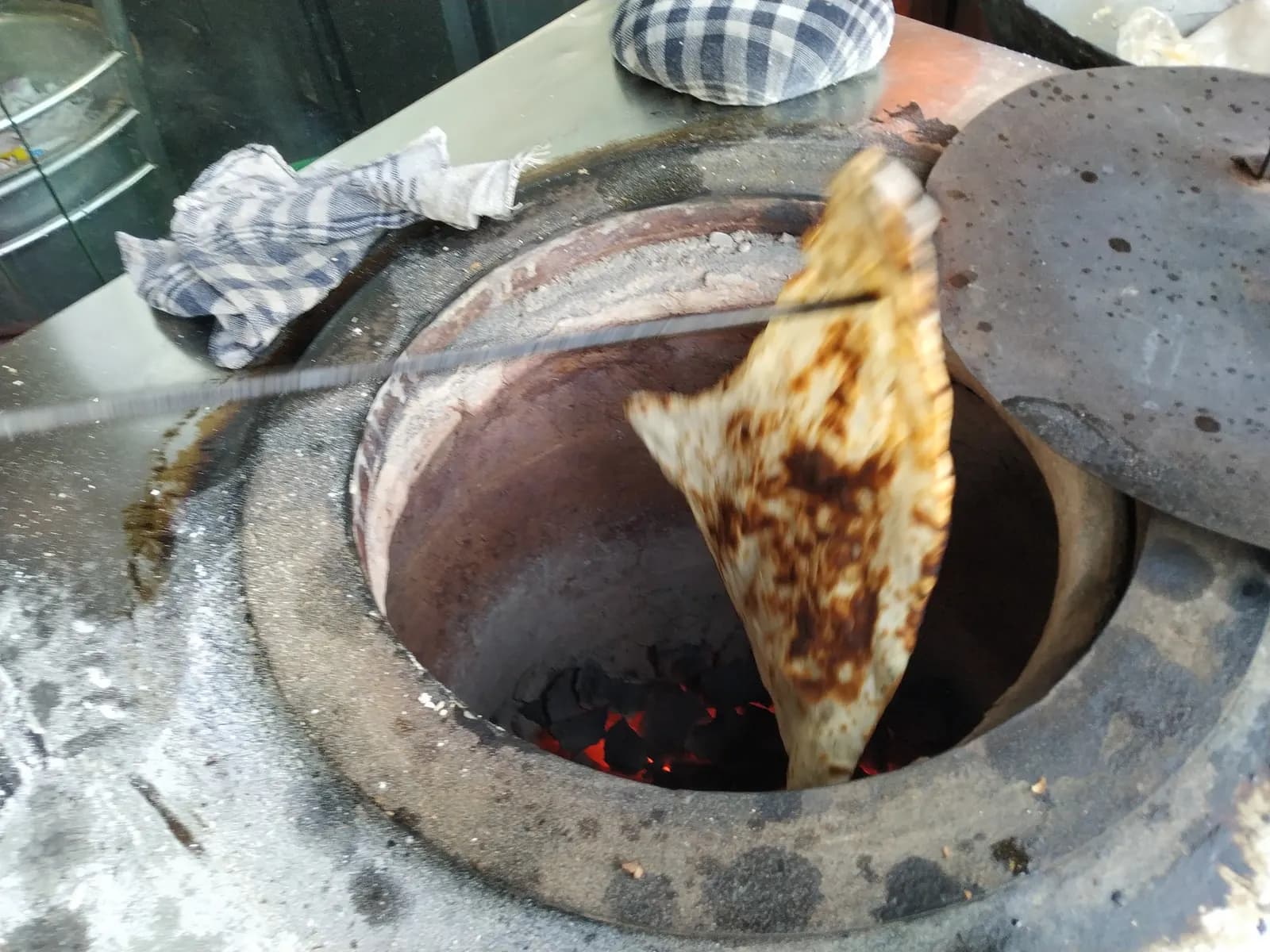 Naan flatbreads stuck to the inner wall of a hot clay tandoor in an Indian kitchen