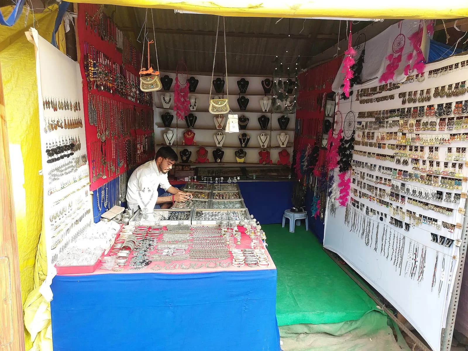 A costume jewellery stall at Shilparamam, Hyderabad, with necklaces on display busts, earrings pinned on boards and bangles on a blue counter