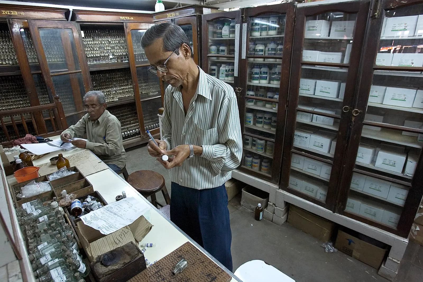 Inside a traditional pharmacy in Varanasi, with wooden cabinets of medicines and two staff at the counter