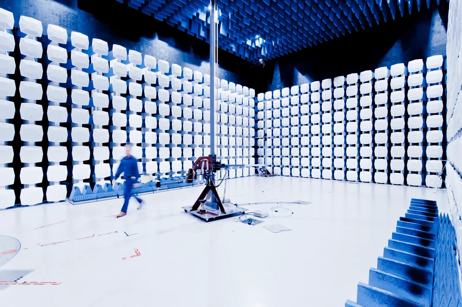 A large anechoic chamber lined with white foam absorbers, with an antenna mast on a turntable for EMC testing